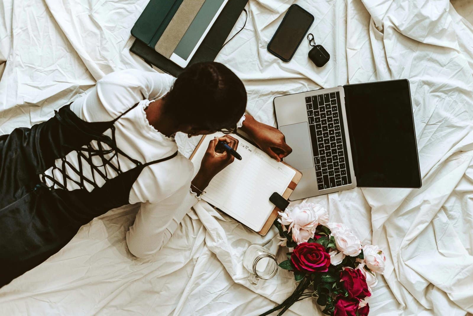 African woman working on her content strategy as part of her content marketing plan remotely on laptop with notebooks and flowers around. Comfortable home setup.