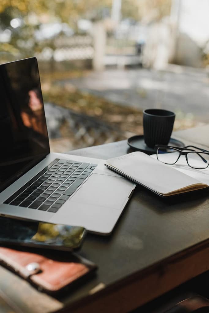 A serene office setup with a laptop, notebook, and coffee near a window, reflecting an autumn scene.