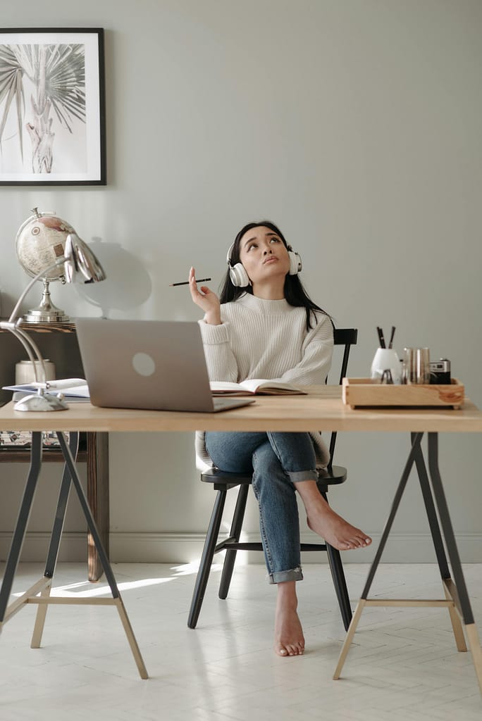Woman sitting at a desk, wearing headphones, thinking deeply with a pencil in hand.